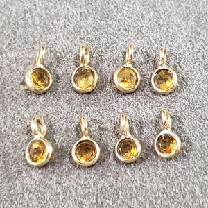 May include: Ten gold-toned charms with small round yellow gemstones. Each charm has a loop for attaching to a necklace or bracelet.