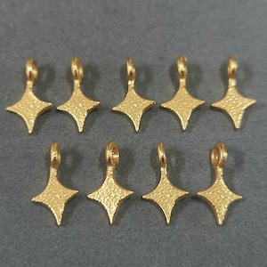 Könnte beinhalten: Zehn goldfarbene Metall-Stern-Anhänger mit strukturierter Oberfläche. Jeder Anhänger hat eine Öse oben zum Anbringen an Schmuck oder andere Bastelarbeiten.