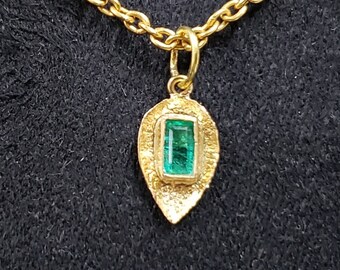 May include: A gold chain necklace with a pendant featuring a green emerald gemstone set in a gold leaf-shaped frame.