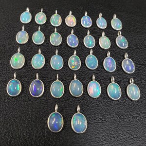 May include: A collection of 27 oval-shaped opal pendants with silver settings. The opals are iridescent with shades of blue, green, and white.