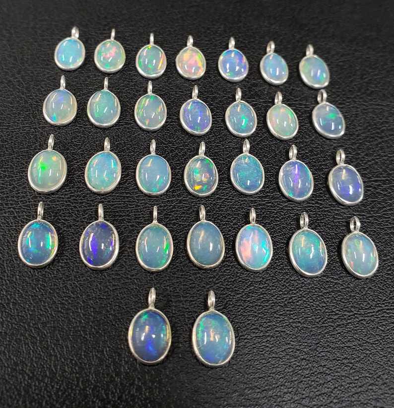 May include: A collection of 27 oval-shaped opal pendants with silver settings. The opals are iridescent with shades of blue, green, and white.
