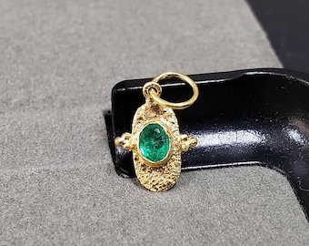 May include: A gold pendant with a textured design features a green emerald gemstone. The pendant has a loop for attaching a chain.