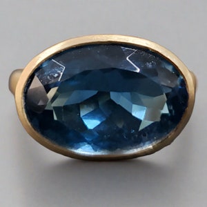 Könnte beinhalten: Ein goldener Ring mit einem großen, ovalen blauen Topas-Edelstein.