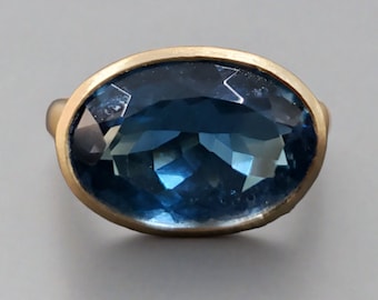May include: A gold ring with a large, oval-shaped blue topaz gemstone.