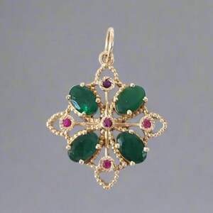 May include: A gold pendant with a floral design. The pendant features four large, oval-shaped green gemstones and five smaller, round red gemstones. The pendant is suspended from a small loop at the top.