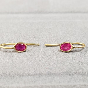 Może przedstawiać: Para złotych kolczyków z małymi owalnymi rubinami.