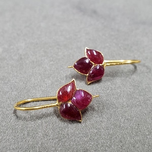May include: A pair of gold earrings with a flower design. Each earring features three red gemstones in the shape of petals.