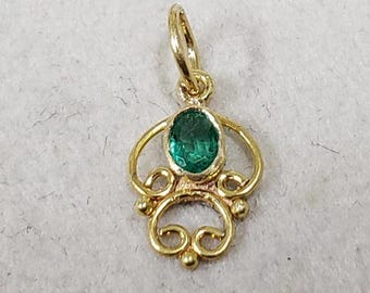 May include: A gold pendant with a green gemstone set in a delicate, ornate design. The pendant features a bail for attaching to a chain.