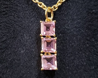 May include: A gold chain necklace with a pendant featuring three pink square-shaped gemstones.
