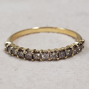Puede incluir: Un anillo de banda de oro con una fila de pequeños diamantes de forma cuadrada.
