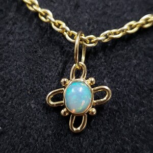 May include: A gold chain necklace with a pendant featuring a round opal gemstone set in a gold four-leaf clover design.
