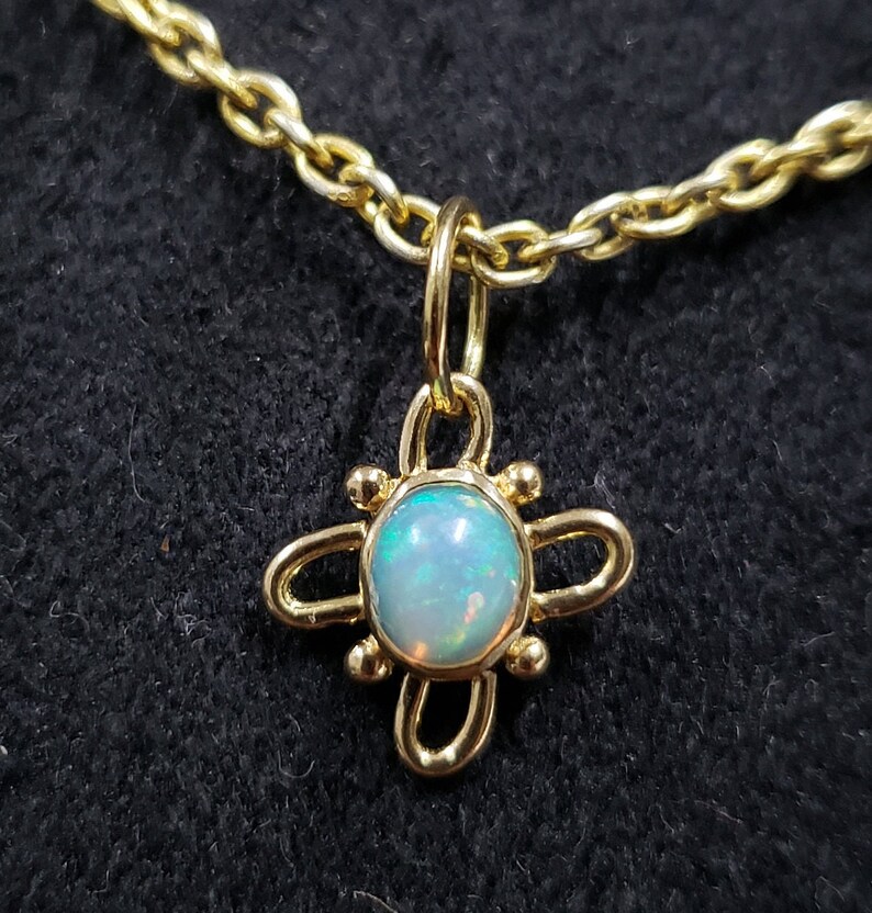 May include: A gold chain necklace with a pendant featuring a round opal gemstone set in a gold four-leaf clover design.