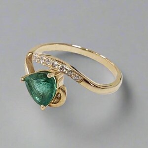 Elegant gold emerald diamond ring with pear cut gemstone on neutral background