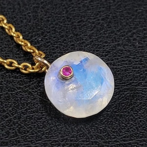 May include: A gold chain necklace with a round moonstone pendant accented with a small pink gemstone.