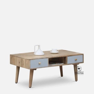 Könnte beinhalten: Ein Couchtisch aus hellem Holz mit zwei Schubladen und einem Regal. Die Schubladen sind hellblau lackiert und haben Holzknöpfe. Der Tisch hat vier Holzbeine.