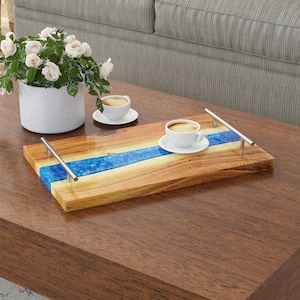 May include: A wooden serving tray with a blue resin inlay and silver handles. The tray is on a wooden table with two white coffee cups and saucers.