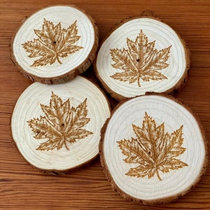 Può includere: Quattro sottobicchieri in legno con un design a foglia d'acero marrone. I sottobicchieri sono realizzati in legno naturale e hanno un aspetto rustico.