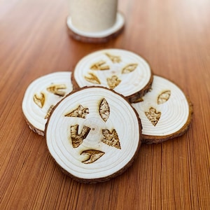 Op de afbeelding: Set van vier houten onderzetters met een natuurlijke houten afwerking. Elke onderzetter heeft een ander ontwerp van een pijlpunt dat in het oppervlak is gegraveerd.