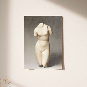 May include: A white marble sculpture of a headless female torso. The sculpture is standing on a gray background.
