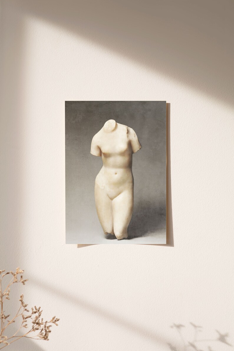 May include: A white marble sculpture of a headless female torso. The sculpture is standing on a gray background.