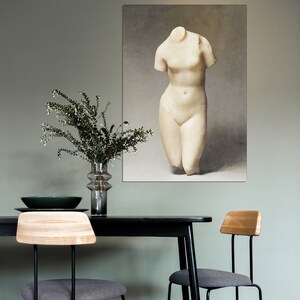 May include: A black dining table with two gray chairs and a vase of greenery. A framed print of a white marble statue of a woman's torso hangs on the wall behind the table.