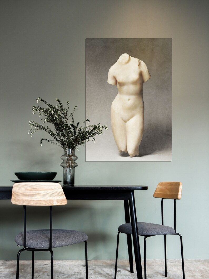 May include: A black dining table with two gray chairs and a vase of greenery. A framed print of a white marble statue of a woman's torso hangs on the wall behind the table.