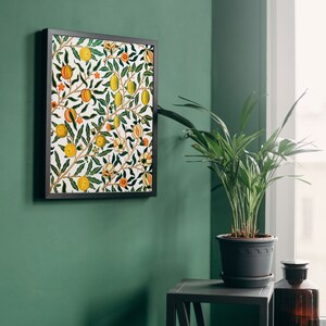 Puede incluir: Una impresi&oacute;n enmarcada de una ilustraci&oacute;n bot&aacute;nica vintage con un patr&oacute;n repetitivo de limones, naranjas y flores sobre un fondo blanco. La impresi&oacute;n est&aacute; colgada en una pared verde junto a una planta en maceta y una mesa peque&ntilde;a.