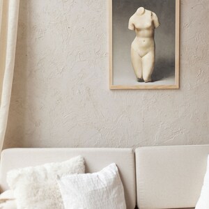 May include: A white plaster sculpture of a female torso in a wooden frame against a textured beige wall. The sculpture is on a white background.