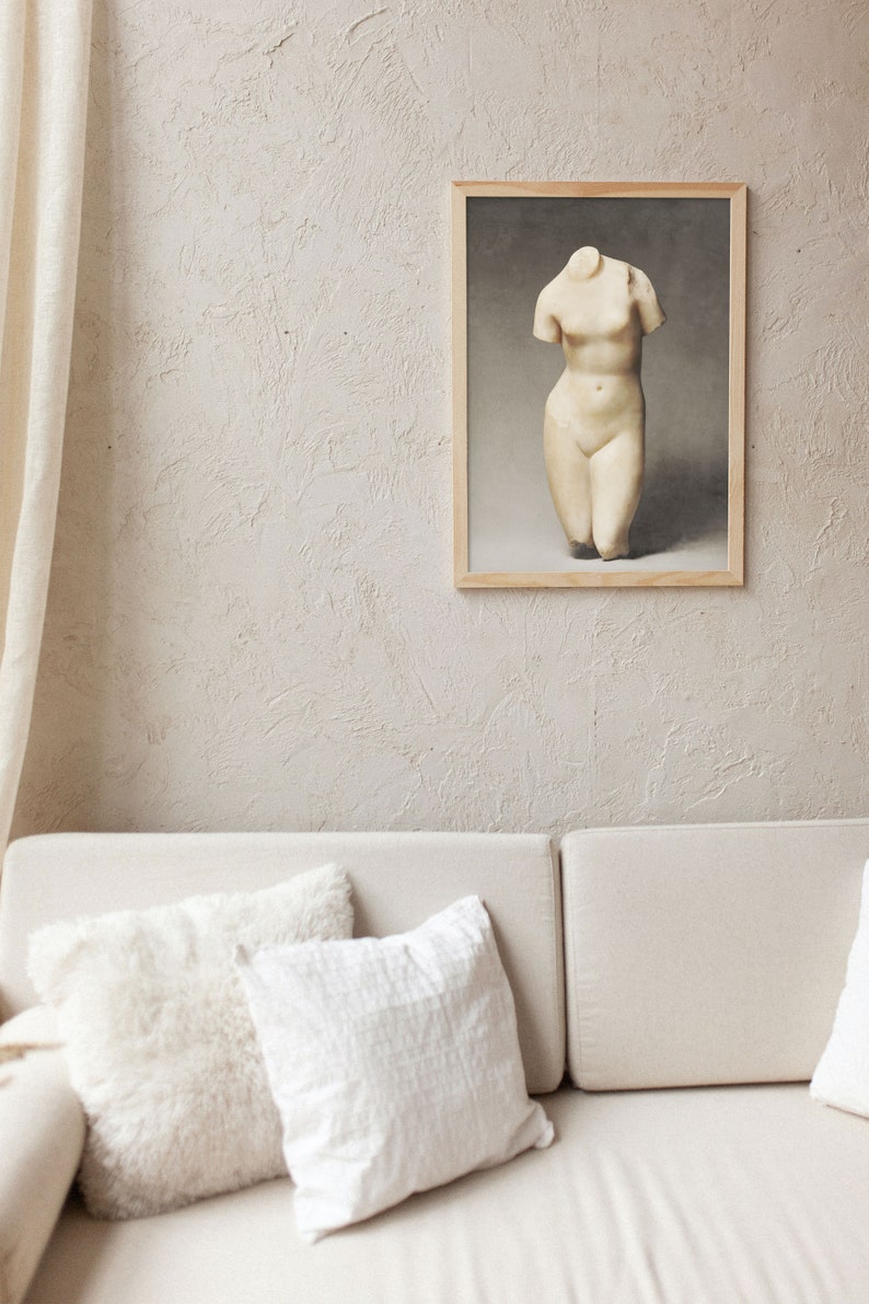 May include: A white plaster sculpture of a female torso in a wooden frame against a textured beige wall. The sculpture is on a white background.
