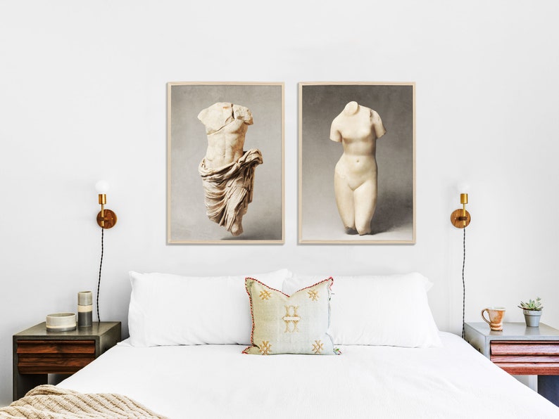 May include: Two framed prints of white marble sculptures of torsos, one male and one female, against a white wall with a bed in the foreground.