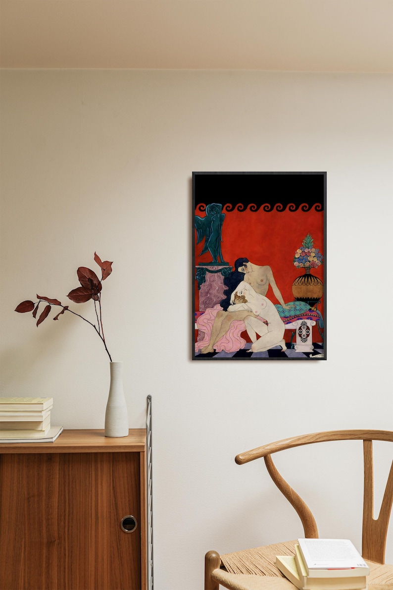 Framed George Barbier Art Deco print hanging above a wooden cabinet in a modern minimalist room. The erotic vintage illustration shows two nude women in an intimate embrace, with rich red tones and classical motifs, ideal for sophisticated boudoir or eclectic art spaces.