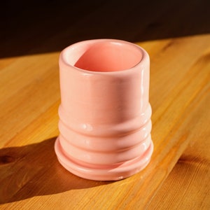 Puede incluir: Una maceta de cer&aacute;mica rosa con un dise&ntilde;o texturizado y acanalado. La maceta tiene una abertura redonda ancha y una base ligeramente acampanada.