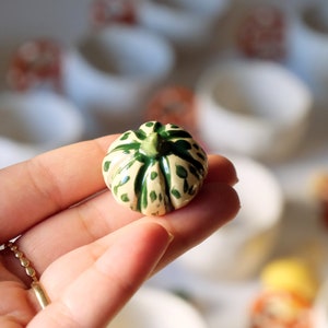 May include: A small ceramic pumpkin with a green and white speckled design. The pumpkin is hand-painted and has a detailed stem.