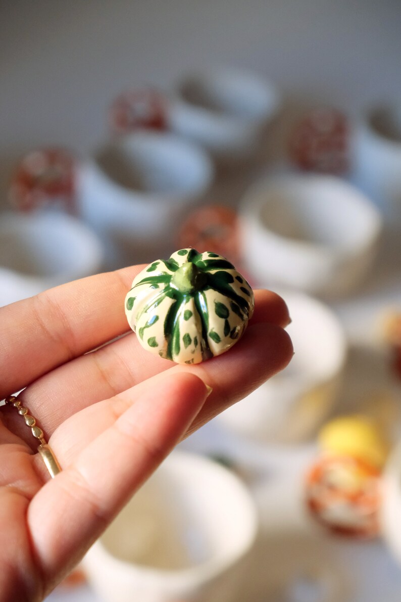 May include: A small ceramic pumpkin with a green and white speckled design. The pumpkin is hand-painted and has a detailed stem.