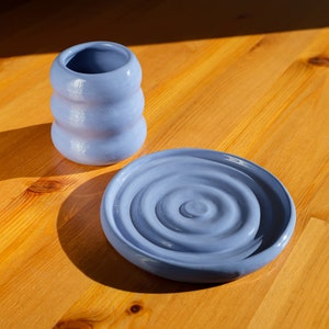 Puede incluir: Un juego de dos platos de cer&aacute;mica azul. El plato m&aacute;s grande tiene un patr&oacute;n de remolino y el plato m&aacute;s peque&ntilde;o es de forma cil&iacute;ndrica.