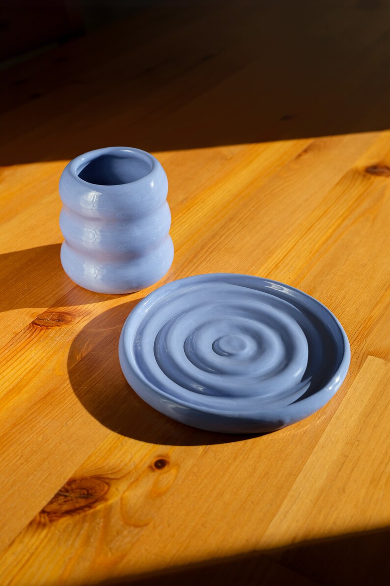 Puede incluir: Un juego de dos platos de cer&aacute;mica azul. El plato m&aacute;s grande tiene un patr&oacute;n de remolino y el plato m&aacute;s peque&ntilde;o es de forma cil&iacute;ndrica.