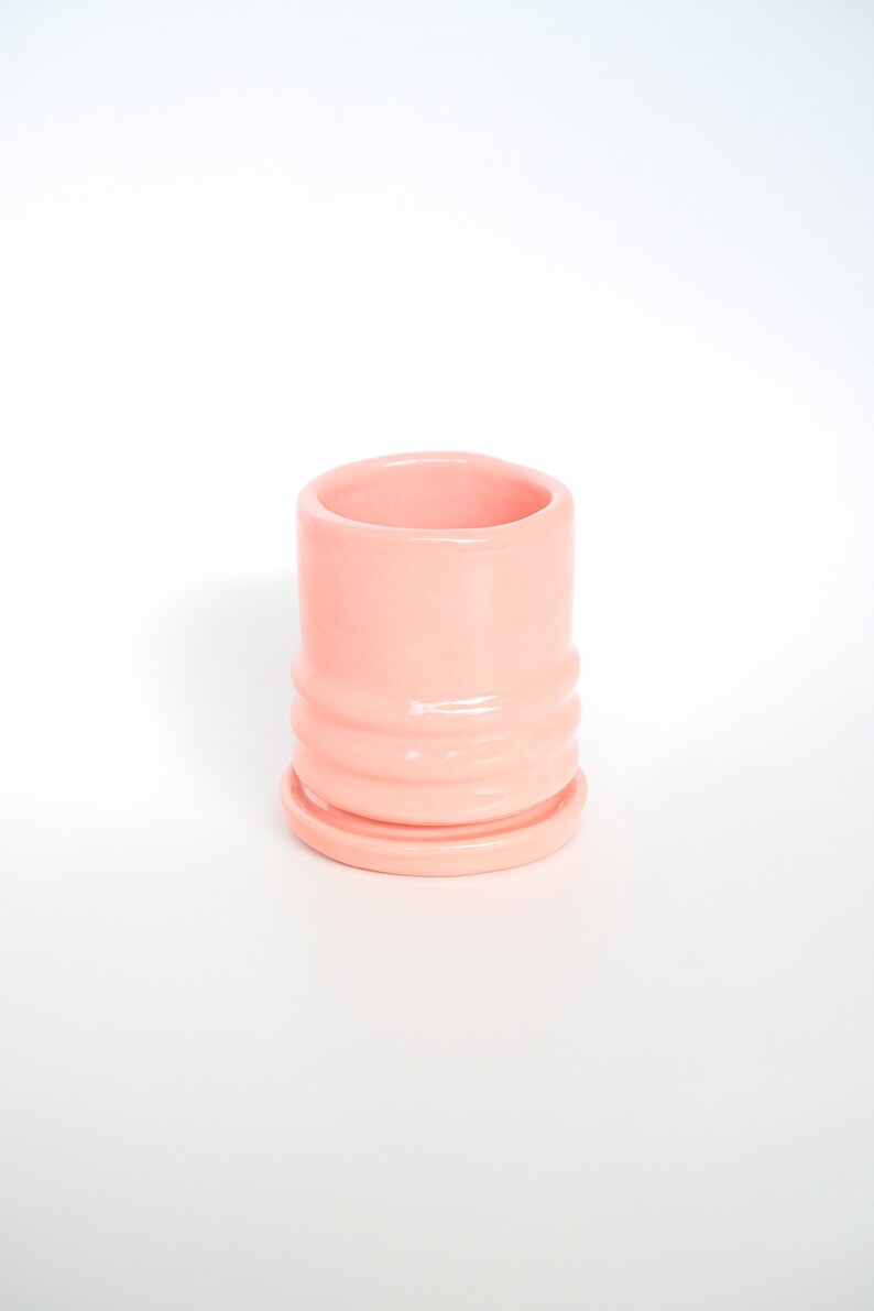 Puede incluir: Una maceta de cer&aacute;mica rosa p&aacute;lido con un dise&ntilde;o acanalado y un platillo a juego. La maceta est&aacute; vac&iacute;a.