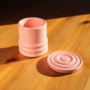 Puede incluir: Un recipiente de cer&aacute;mica rosa con tapa. El recipiente tiene un dise&ntilde;o acanalado y la tapa tiene un patr&oacute;n circular.