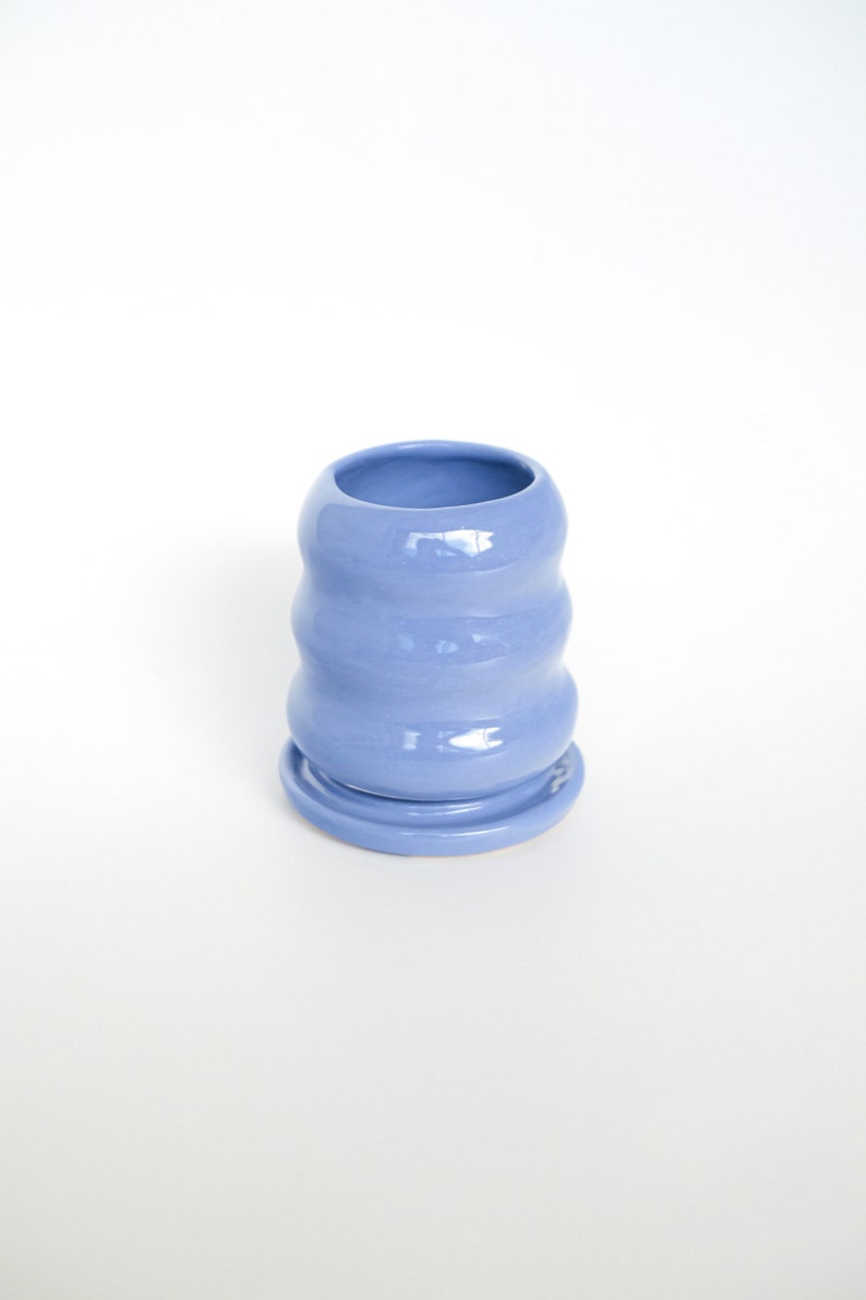 Puede incluir: Una maceta de cer&aacute;mica azul claro con un dise&ntilde;o ondulado y un platillo a juego. La maceta est&aacute; vac&iacute;a y lista para una planta.