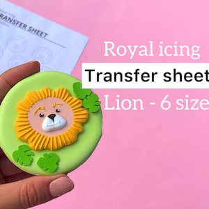 May include: A green cookie decorated with a yellow lion face and green leaves. The cookie is being held by a hand. The text "Royal icing Transfer sheets Lion - 6 sizes" is visible in the background.