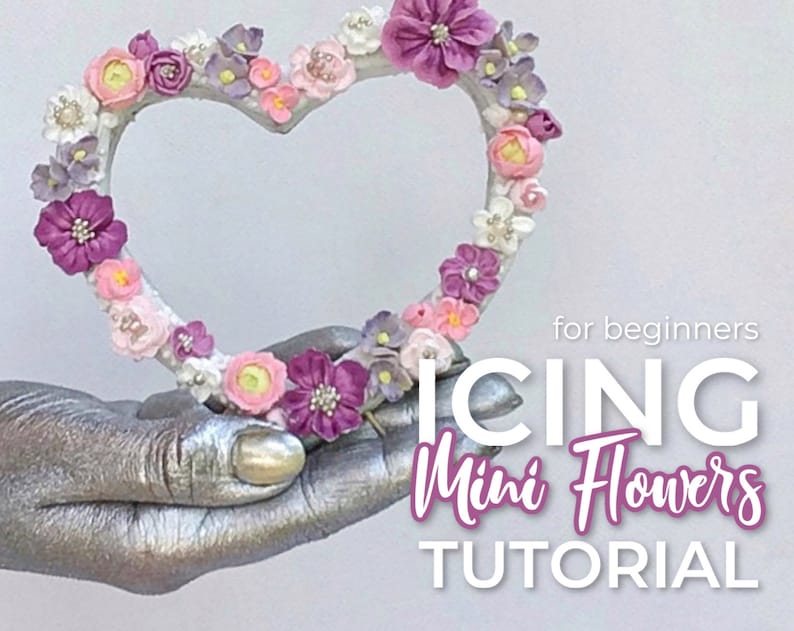 K&ouml;nnte beinhalten: Ein herzf&ouml;rmiger Kranz, der mit rosa, lila und wei&szlig;en Zuckerblumen verziert ist. Der Text "for beginners ICING Mini Flowers TUTORIAL" befindet sich unter dem Kranz.