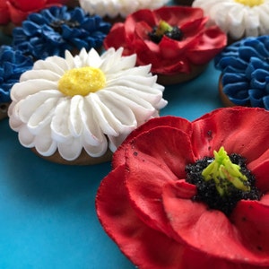May include: Assortment of decorated sugar cookies with red, white, and blue frosting. The cookies are shaped like flowers, including daisies, poppies, and blue flowers.