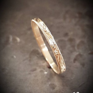 May include: A thin gold band with an intricate floral design engraved around the entire band.