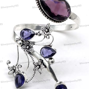 May include: A silver-toned bracelet with multiple purple gemstones and floral accents. The bracelet features a large, oval-shaped purple stone and several smaller teardrop-shaped stones. The design includes intricate floral details, creating an elegant and artistic piece.