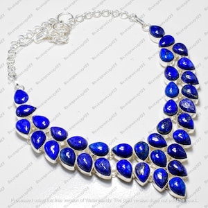May include: A silver necklace featuring multiple rows of vibrant blue lapis lazuli gemstones. The teardrop-shaped stones are set in silver and connected by a delicate chain. The jewelry is displayed on a white surface.