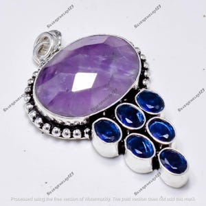 May include: A silver pendant with a large, faceted purple amethyst and smaller blue gemstones. The pendant has a decorative silver setting with a beaded border. The text "SILVERJEWELRY123" is visible.