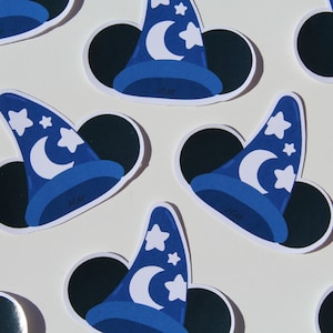 May include: A pattern of stickers featuring a blue wizard hat with a white crescent moon and stars. The hat is set against a black circle, with the initials "M.M." visible on the hat.