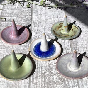 Puede incluir: Cinco porta anillos de cerámica en diferentes colores y patrones. Los porta anillos tienen todos la forma de un cono con una pequeña base. Los colores incluyen rosa, azul, verde y gris.