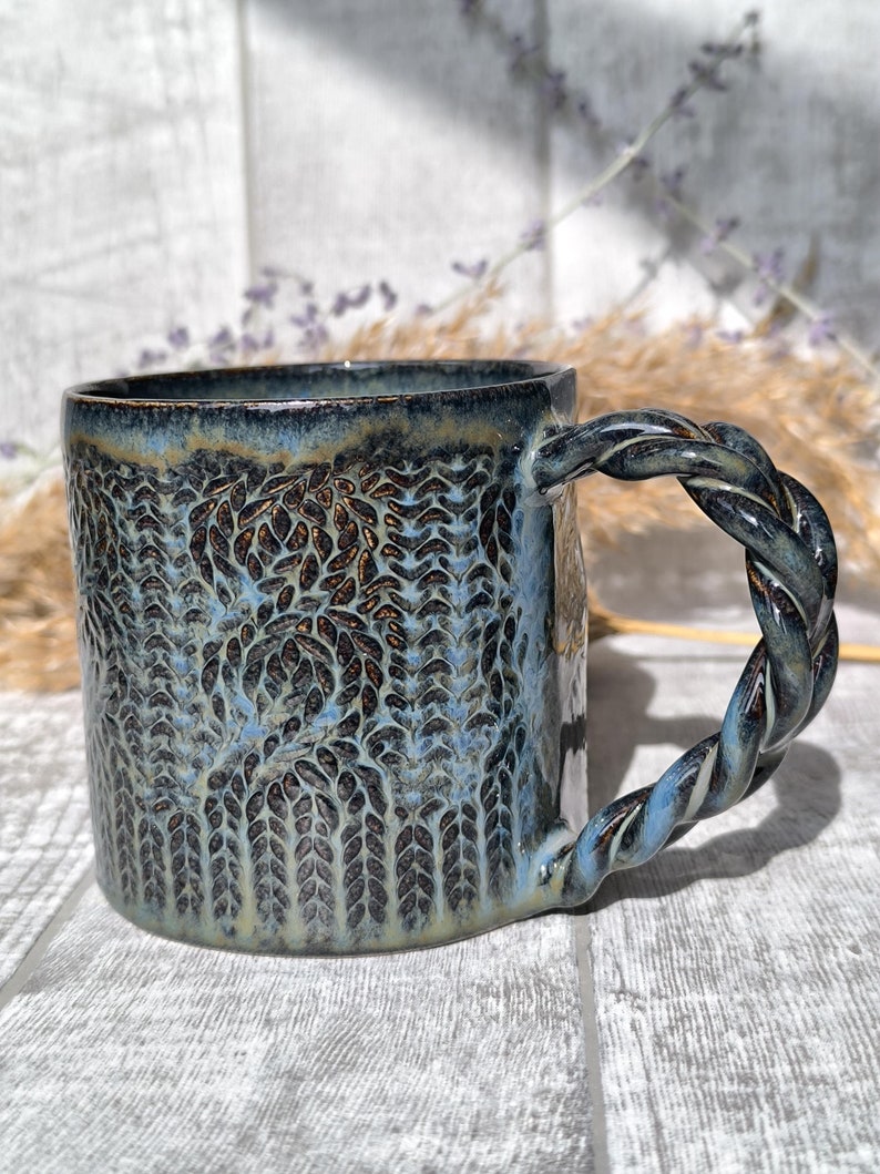 May include: A blue ceramic mug with a textured, leaf-like design and a twisted rope handle.