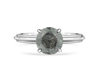 Puede incluir: Un anillo de plata con un diamante redondo, gris y facetado.
